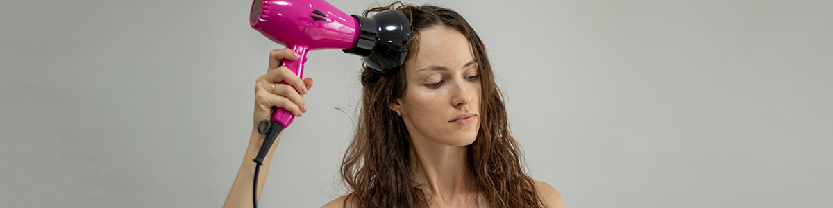 Kobieta suszy kręcone włosy czarnym dyfuzorem na tle jasnej ściany.