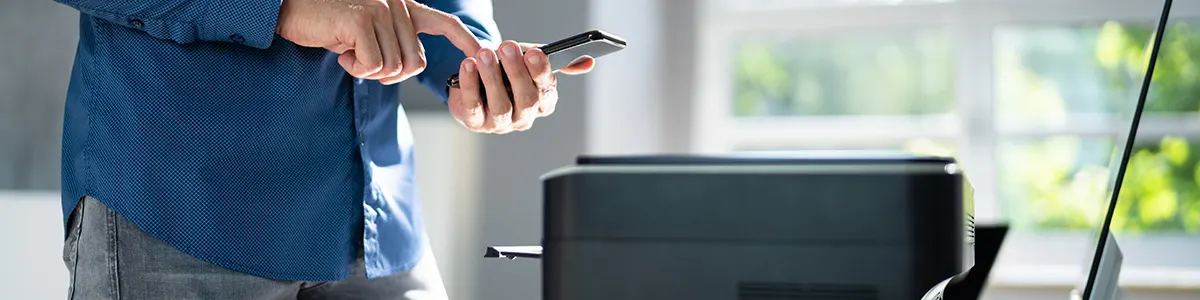 Mężczyzna stoi ze smartfonem w dłoni i łączy telefon z drukarką.