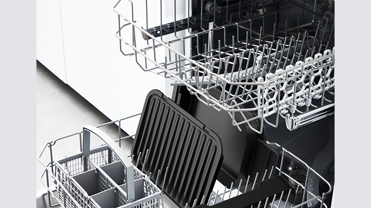 Wnętrze zmywarki z metalowymi koszami na naczynia, w dolnym koszu czarna blacha do pieczenia i pojemnik na sztućce.