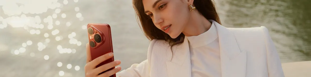 Kobieta w białej marynarce na tle jeziora robi wertykalne zdjęcie czerwonym telefonem Huawei Pura 80 Pro.