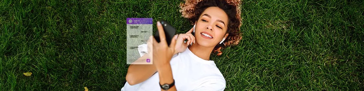 Dziewczyna leży na trawie ze słuchawkami w uszach i robi print screen na swoim smartfonie.