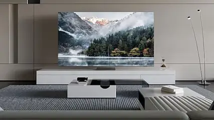 Salon z telewizorem pokazującym górski krajobraz, białe meble i szary dywan. Stojąca lampa z tyłu.