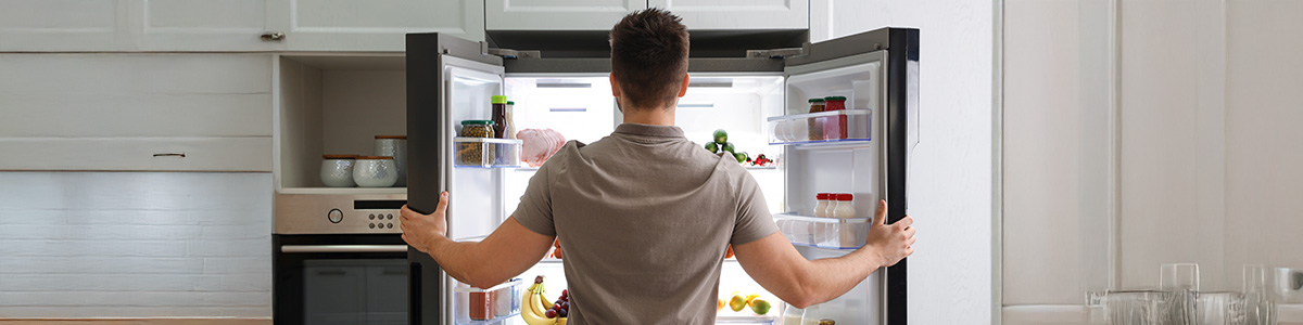 Mężczyzna zagląda do otwartej lodówki side by side.