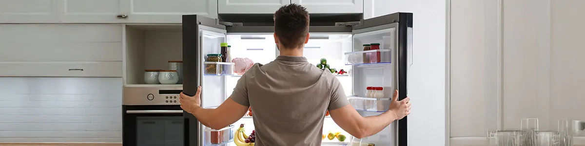 Mężczyzna zagląda do otwartej lodówki side by side.