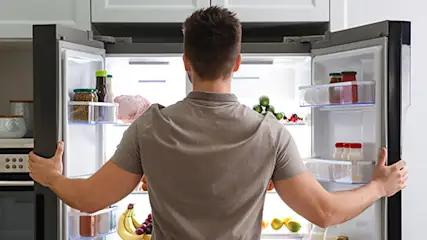 Mężczyzna zagląda do otwartej lodówki side by side.