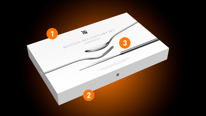 Białe pudełko z zestawem sztućców WMF. Na pudełku narysowane sztućce: łyżka, widelec, nóż. Tło jest czarno-pomarańczowe.