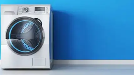 Biała pralka stoi na białej listwie przypodłogowej na tle niebieskiej ściany.