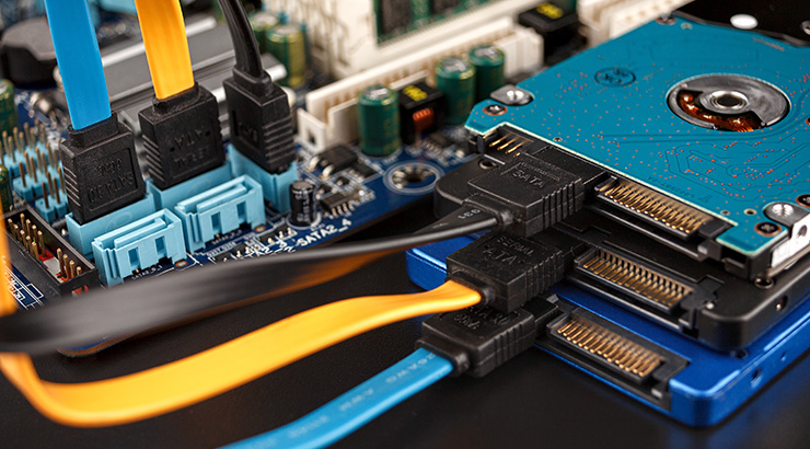 Widok z bliska na płytę główną komputera z podłączonymi niebieskimi, żółtymi i czarnymi kablami SATA do niebieskiego dysku twardego.