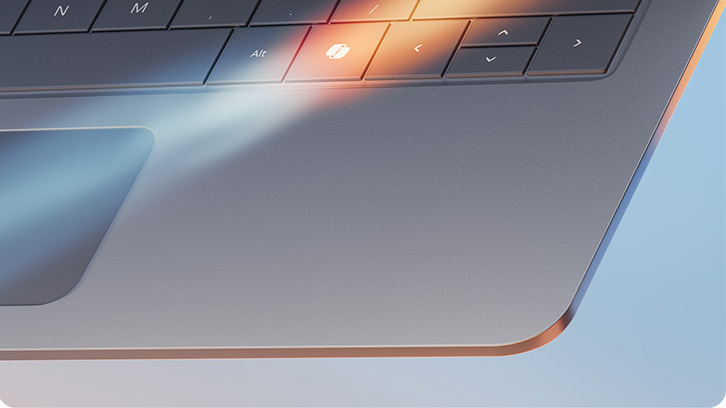 Fragment szarego laptopa z klawiaturą i touchpadem, oświetlony światłem. Widoczne klawisze ze strzałkami.