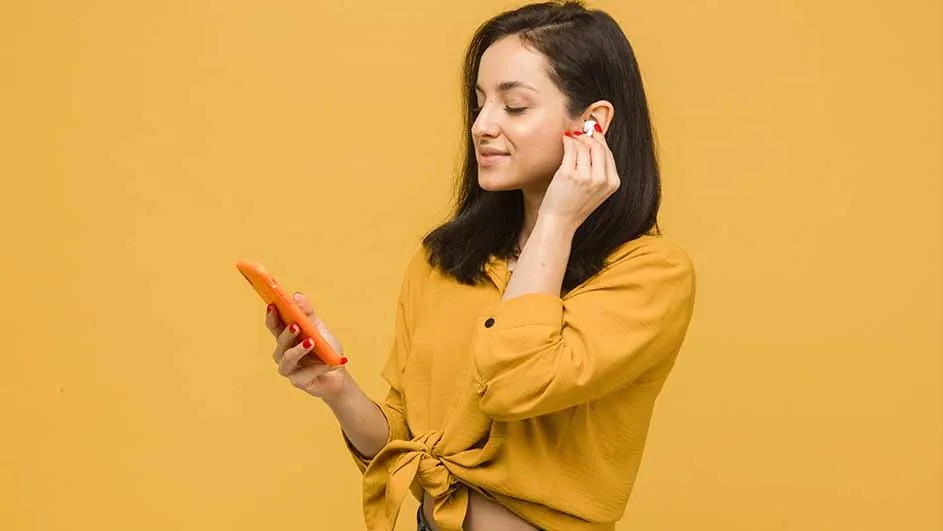 Kobieta w żółtej koszuli z telefonem wkłada słuchawkę do ucha na żółtym tle.