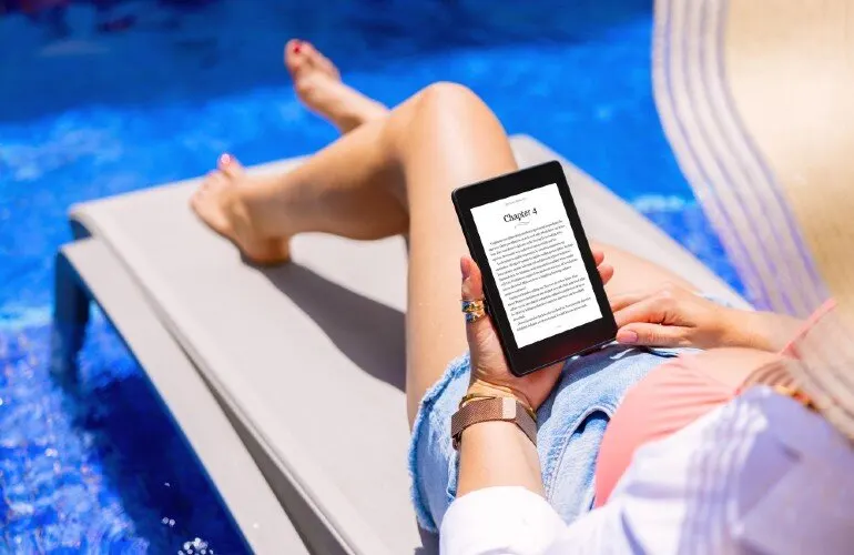 Osoba czyta e-booka na leżaku obok basenu. Na ekranie widnieje tekst "Rozdział 4".