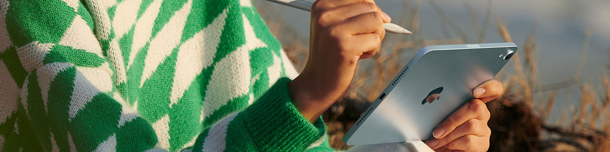 Osoba w zielono-białym swetrze trzyma iPada oraz rysik Apple Pencil