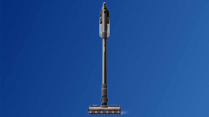 Na niebieskim tle stoi pionowo szary odkurzacz akumulatorowy z przezroczystym pojemnikiem na kurz i podświetlaną szczotką.