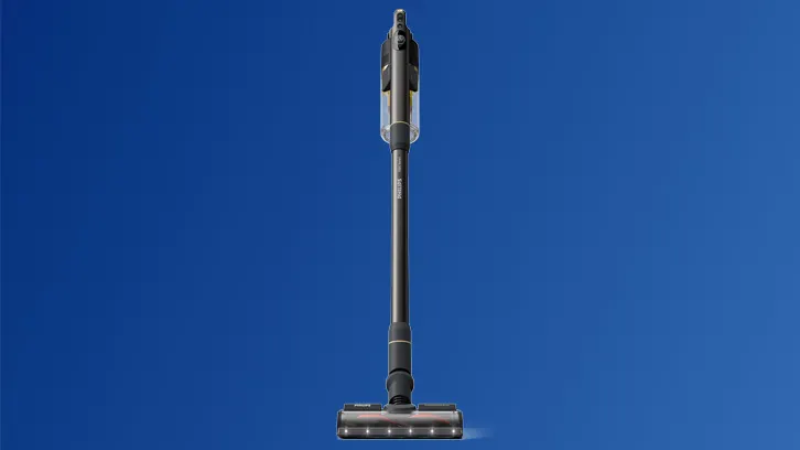 Na niebieskim tle stoi pionowo szary odkurzacz akumulatorowy z przezroczystym pojemnikiem na kurz i podświetlaną szczotką.