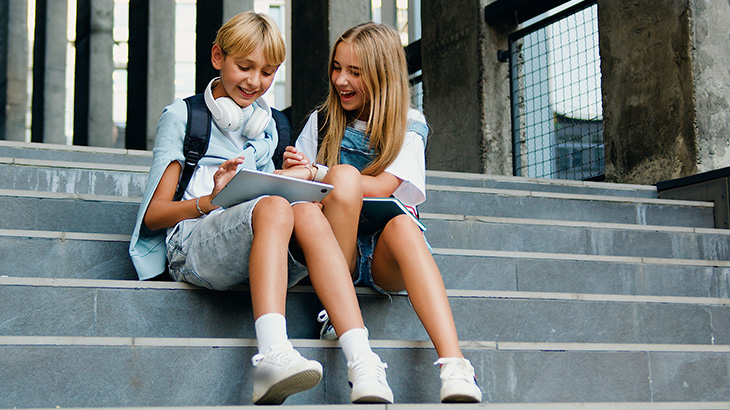 Dwójka dzieci siedzi na schodach i klikają w tablet do nauki