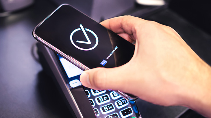 Ręka trzymająca smartfon, płacąca zbliżeniowo na terminalu płatniczym 