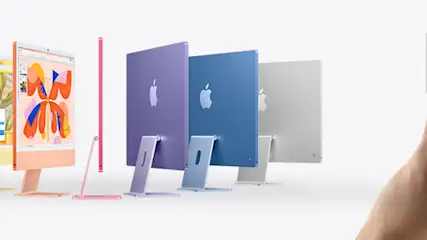 Na zdjęciu widać rząd kolorowych komputerów iMac obok dłoni trzymającej srebrny komputer Mac Studio.