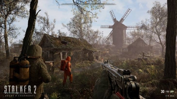 Na obrazie widoczny mężczyzna w kombinezonie ochronnym i z bronią w zaroślach, w tle widać budynki i wiatrak.