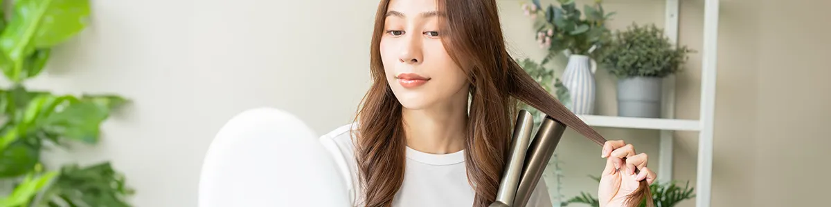 Dziewczyna modelująca swoją fryzurę lokówką do włosów stojąc przed lustrem.