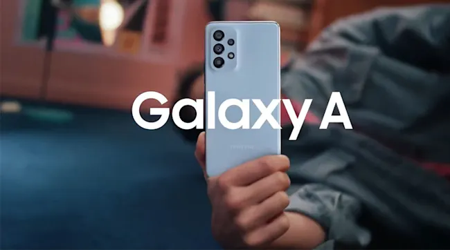 Osoba trzyma jasnoniebieski telefon Samsung Galaxy A z trzema obiektywami aparatu. Z przodu widoczny biały napis Galaxy A.