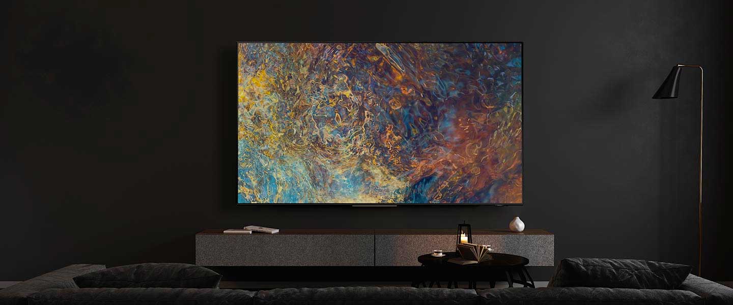 Salon z telewizorem z abstrakcyjnym obrazem na ścianie. Pod telewizorem szafka, na niej książki i wazon. Obok lampa podłogowa.