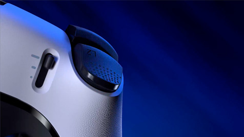 Na pierwszym planie kontroler do gier w odcieniach bieli i czerni na niebieskim tle. Widoczny przycisk i przełącznik.