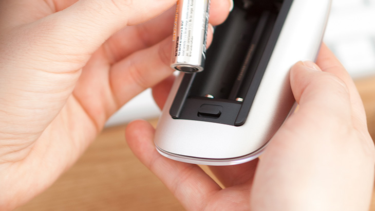 Ręce wkładają baterię AA do białej ładowarki na drewnianym stole.