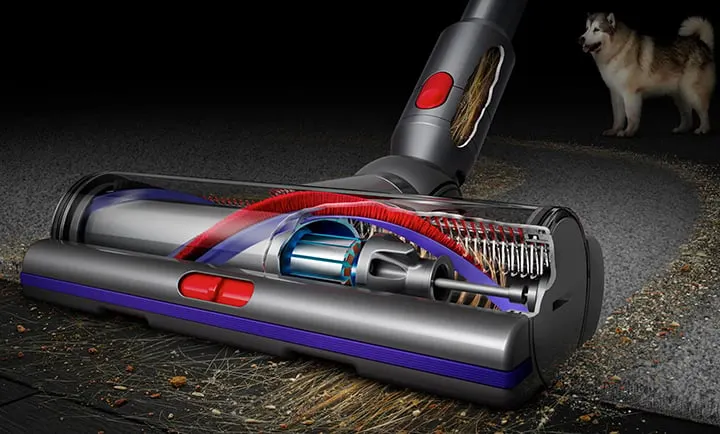 Przekrój poprzeczny odkurzacza na dywanie, w tle pies. Widoczne elementy wewnętrzne: silnik, szczotki, czerwone i niebieskie akcenty.