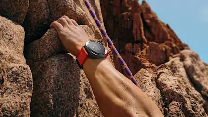 Osoba wspina się po skałach, używając liny. Na nadgarstku ma zegarek z czerwonym paskiem.