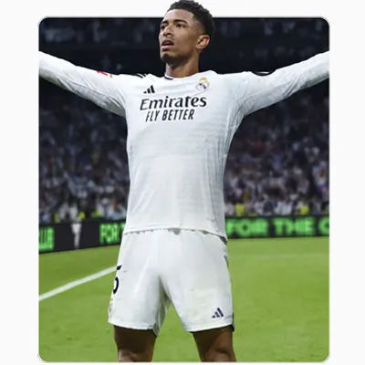 Na pierwszym planie piłkarz w białym stroju z rozłożonymi ramionami, na zielonym boisku, z widownią w tle.