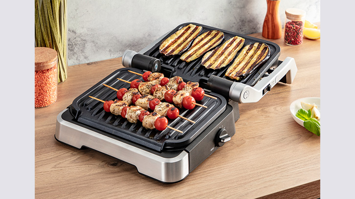 Grill elektryczny z grillowanymi plastrami bakłażana i szaszłykami z kurczaka z pomidorami na drewnianych patykach.