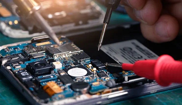 Na zdjęciu widać niebieską płytę główną smartfona z elementami elektronicznymi, narzędzia (śrubokręty) i czerwoną sondę miernika.