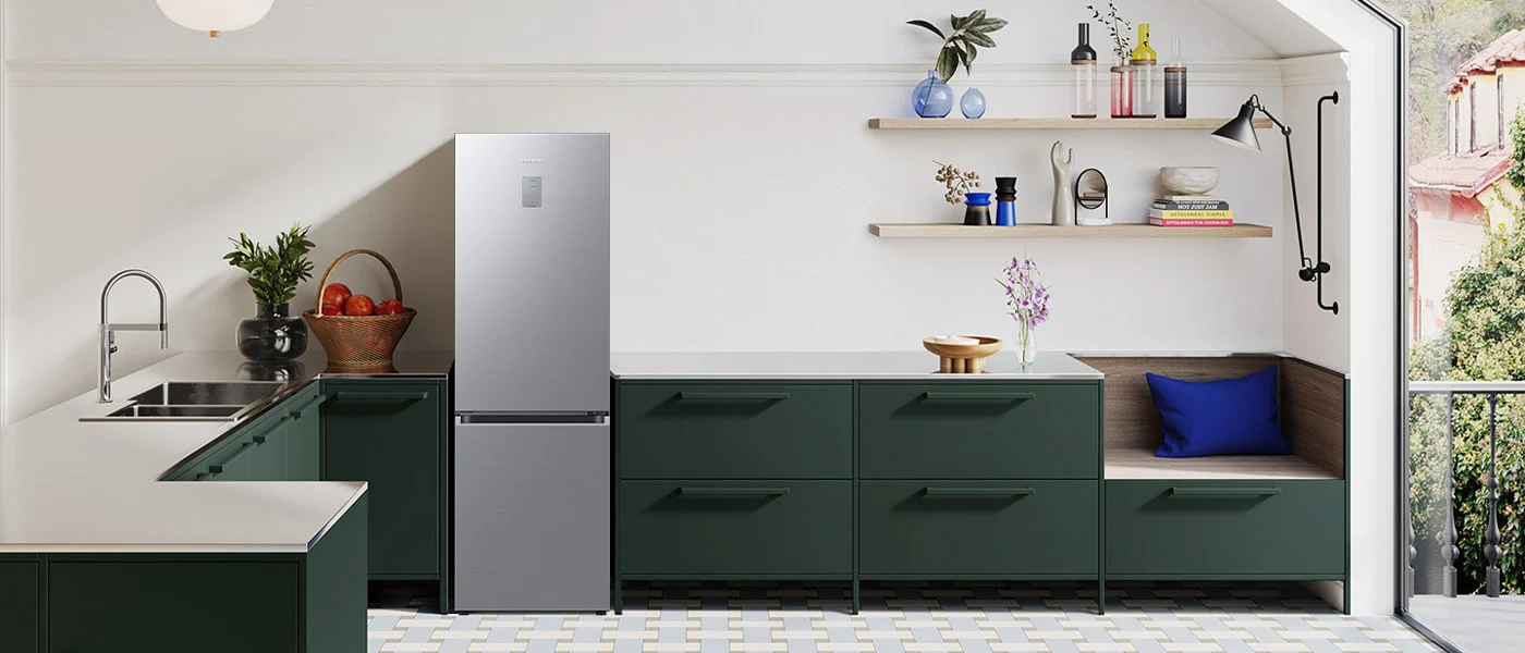 Wnętrze kuchni z zielonymi szafkami, srebrną lodówką i drewnianymi półkami. Na półkach wazony, butelki i dekoracje. Podłoga w biało-szare wzory.