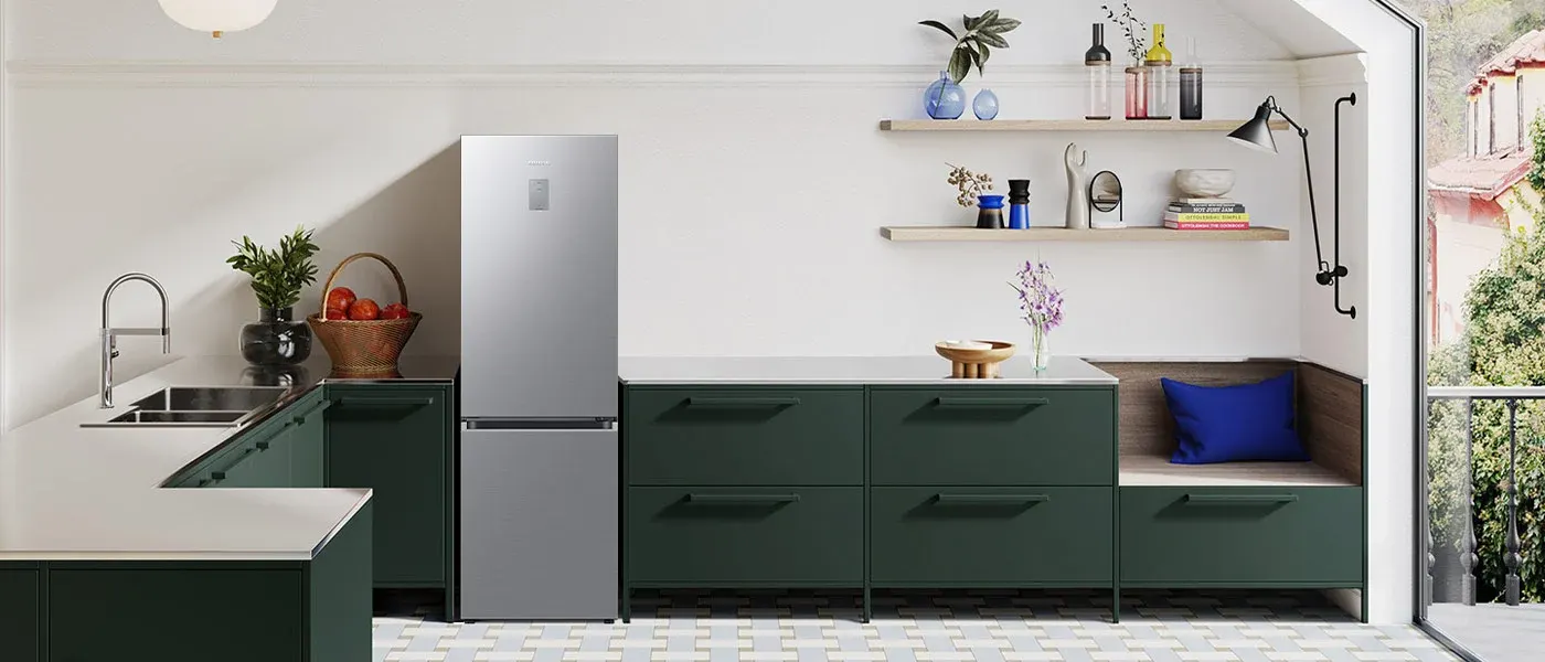 Wnętrze kuchni z zielonymi szafkami, srebrną lodówką i drewnianymi półkami. Na półkach wazony, butelki i dekoracje. Podłoga w biało-szare wzory.