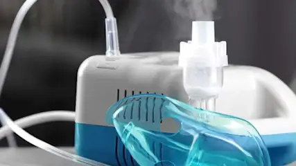 Aparat do inhalacji z maską tlenową i rurką, na stole, z rozmytym tłem.