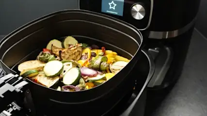 Warzywa w czarnym koszu frytkownicy beztłuszczowej, obok stoi urządzenie z ekranem.