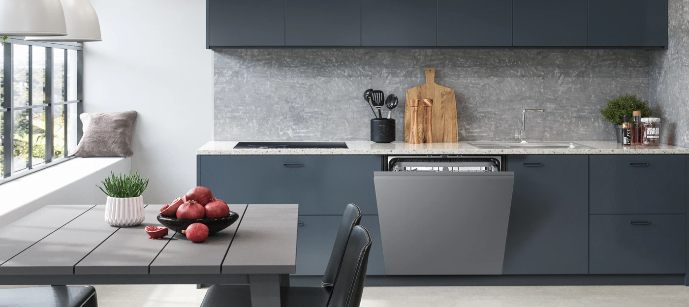 Kuchnia z szarymi szafkami, zmywarką i stołem. Na stole misa z granatami i doniczka z zieloną rośliną.