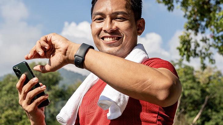 Mężczyzna podczas treningu w terenie, z ręcznikiem na karku, spogląda na smartwatch z eSIM.