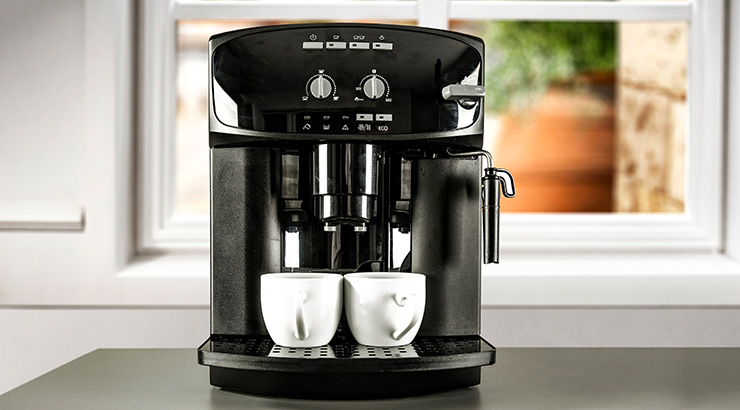 Czarny ekspres do kawy z dwoma białymi filiżankami na tacy ociekowej, na tle okno.