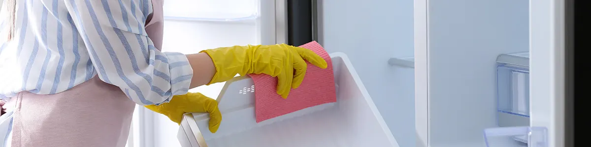 Kobieta w kuchni myjąca lodówkę.