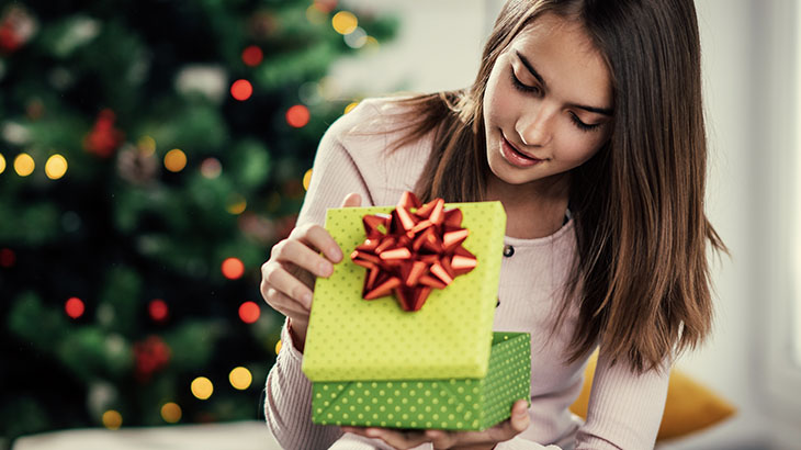 Nastolatka otwierająca zielony prezent w tle choinka.