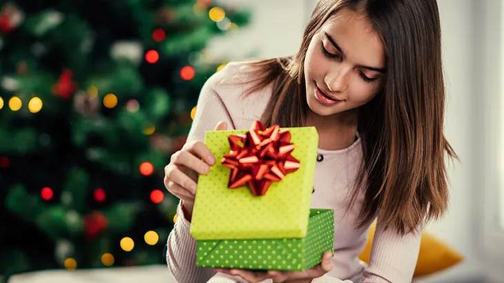 Nastolatka otwierająca zielony prezent w tle choinka.