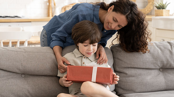 Mama dająca prezent dziecku, które siedzi na kanapie w salonie.