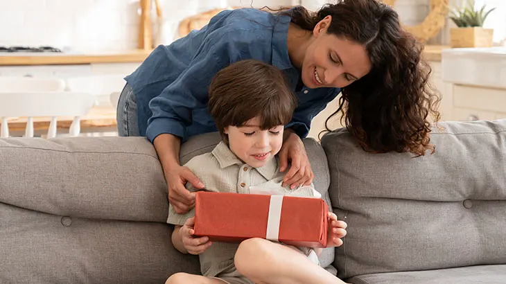 Mama dająca prezent dziecku, które siedzi na kanapie w salonie.