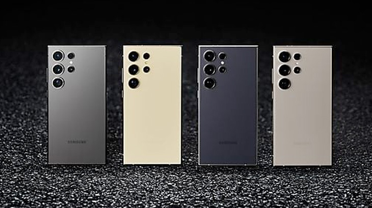 Cztery telefony w odcieniach szarości, beżu i granatu stoją obok siebie na ciemnym, teksturowanym tle. Widoczne są obiektywy aparatów.