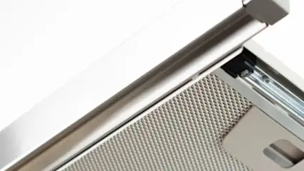 Zdjęcie z dołu ukazuje srebrny okap kuchenny z metalową siatką na tle białego sufitu.