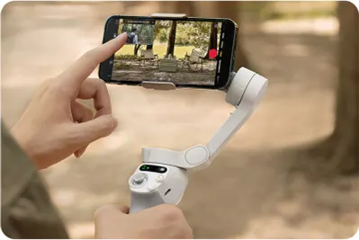 Osoba obsługuje gimbal z telefonem, nagrywając film w plenerze. Na ekranie widoczny film z drzewami i osobą.