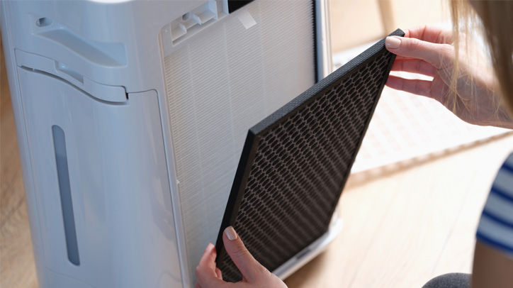 Osoba wymienia czarny filtr w białym oczyszczaczu powietrza w pomieszczeniu.