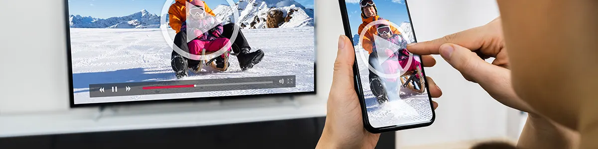 Kobieta trzyma w dłoni smartfon i udostępnia ekran z telefonu na telewizor stojący na komodzie.