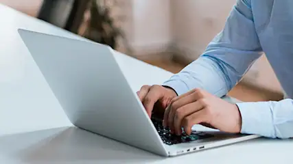 Osoba w niebieskiej koszuli pracuje na laptopie